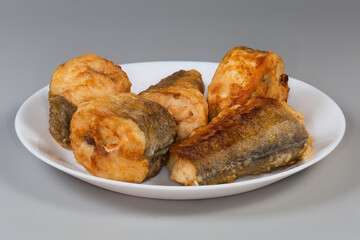 Fried hake pieces on dish on gray background, side view