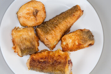 Fried hake pieces on dish on gray background, top view