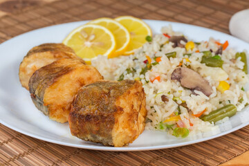 Fried hake hubbsi pieces with rice and vegetables, close-up