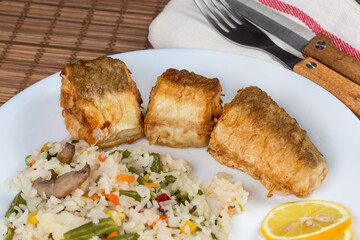 Serving of fried hake hubbsi pieces with rice and vegetables