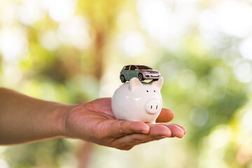 Man hand holding the piggy bank and the car model put on the top on the bokeh background in the public park, Loans for car concept.