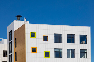 Corner fragment of building with windows of different sizes and ventilated facade made of white composite panels. Modern technology of building facades design