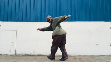 Hipster dancing b-boy foot step at street with blue wall. Asian break dancer practice street dance...