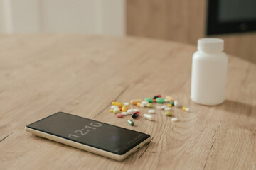 Close-up different pills and alarm clock on the phone on a wooden table. Concept of medicine and healthcare. Part of a series