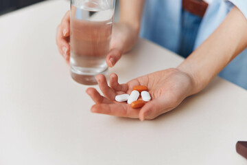 Person holding a bottle of pills and glass of water next to another bottle of pills on a table