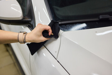 Person using black cloth to clean white cars hood, bumper, and tires