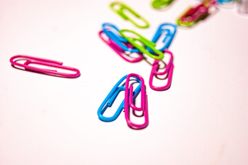 paper clips on white. chaotic, office desk, colorful paper clips scattered across a white surface.