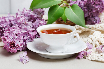 Porcelain cup with tea and lilacs in the background.