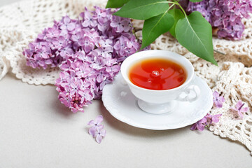 Porcelain cup with tea and lilacs in the background.