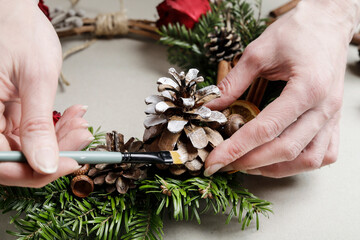 Florist at work: woman shows how to make a Christmas door wreath with roses, fir and cinnamon...