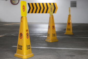 Three yellow cones with black and white writing on them are in a parking lot