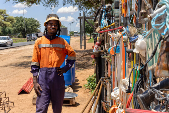 african street vendor selling hardware on the side of the road, wearing orange workwear and dreadlocks braids