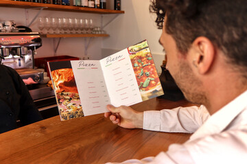 Person choosing food from a menu seen from behind in a pizza restaurant, the menu is visible