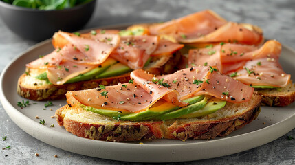 Toasted artisan bread with slices of turkey ham on crushed avocado in a white background