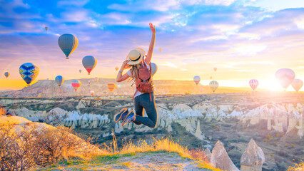 Happy woman jumping in air- beautiful sunrise Cappadocia landscape with hot air balloons flying in...