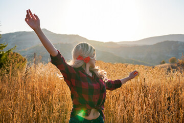 A blonde woman in a plaid shirt stands in a field of tall grass. happy woman outdoors at sunset on...