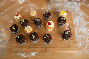 Cupcake, icing and sprinkles on wooden board for eating, birthday party and lunch in house. Muffins, cake and chocolate or vanilla flavor snack for desert, pastry or bakery display with sugar candy