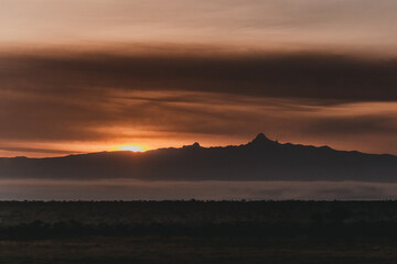 Obraz premium Fiery sunset silhouettes Mount Kenya over misty landscape