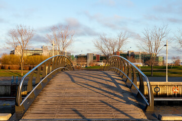 Pedestrian bridge over part of the Louise Basin, with modern and patrimonial buildings in the background seen during an early spring golden hour morning, Quebec City, Quebec, Canada
