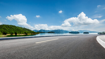 Asphalt highway road and lake with mountains nature landscape on a sunny day. Beautiful coastline...