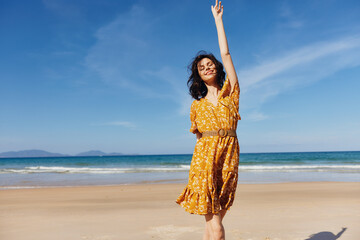 Woman in yellow dress with arms raised standing on beach enjoying sunshine and freedom