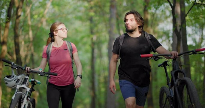 Friends enjoying a leisurely walk with bicycles in a sunlit forest