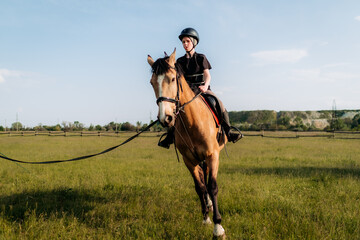 A teenage boy in a helmet learns horse riding in the summer, the instructor teaches the child equestrianism.