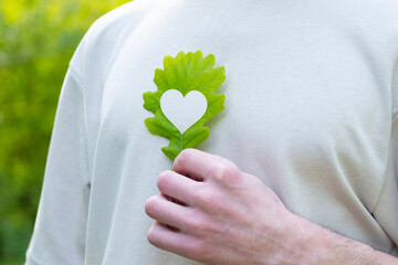 young man holds green heart-shaped leaf close to heart, happiness and health, overall well-being,...