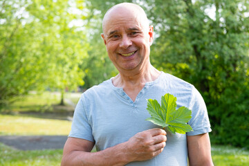 joyful 65-year-old man holds green leaf close to heart, happiness and health, overall well-being, Green living, Nature therapy, healthy lifestyle