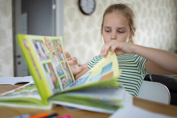 A pretty school-age girl does her homework using a textbook and enters information into a workbook....