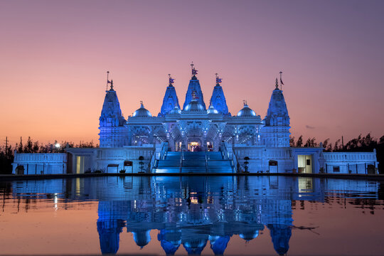 BAPS Shri Swaminarayan Mandir illuminated and reflected against water during sunset