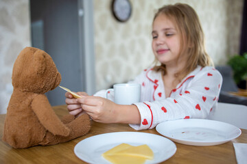 A pretty blonde girl in beautiful pajamas with hearts is having a delicious breakfast and feeding...