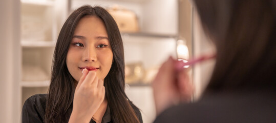 Smiling beautiful asian woman fresh healthy skin looking on mirror and enjoying applying skincare...