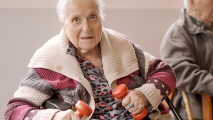 Old woman exercising with dumbbells sitting on a nursing home