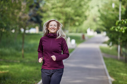 Joyful middle-aged woman running in a lush park, exuding happiness