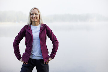 Confident middle-aged woman standing hands-on-hips in a foggy lakeside setting