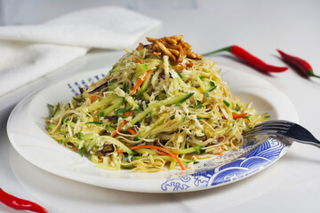 Salad with cabbage, cucumber, carrots, noodles, chicken in a plate on the table