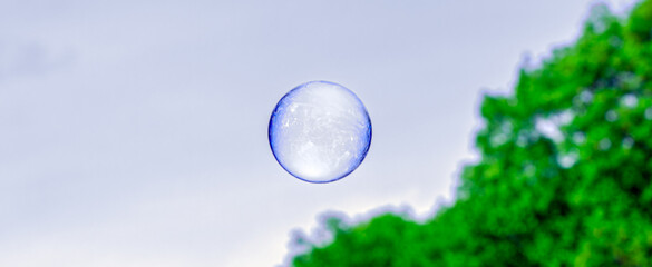 a perfectly round soap bubble of a blue hue, with solar reflection and shimmer of light against a...
