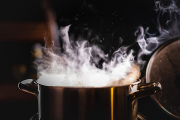 A boiling pot steams up as a chef opens the lid of a cooking pot in a restaurant.