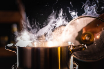 A boiling pot steams up as a chef opens the lid of a cooking pot in a restaurant.
