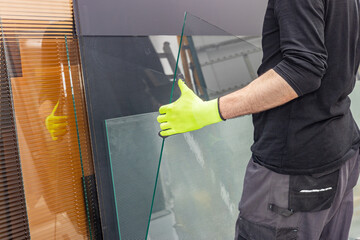 A glazier lifts a glass pane from a rack of glass in a factory