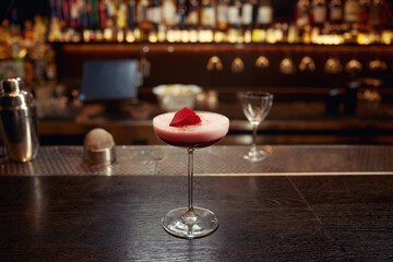 Pink cocktail decorated with rose floral petal on wooden bar counter desk