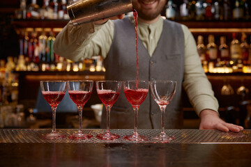 Bartender pouring freshly prepared cocktail into several glasses