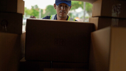 A delivery worker in a cap and safety vest efficiently handling cardboard packages inside a...