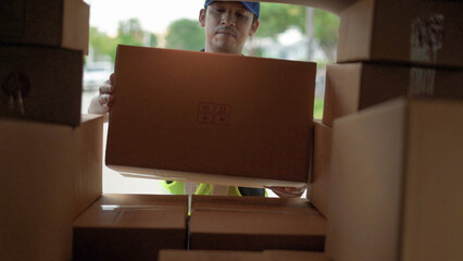 A delivery worker in a cap and safety vest efficiently handling cardboard packages inside a delivery van.
