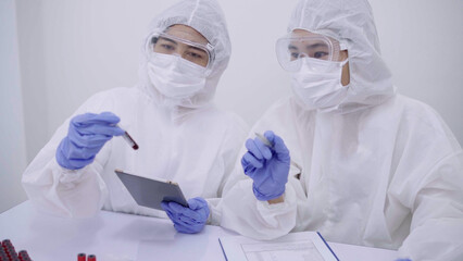 Two scientists dressed in protective gear examining samples and discussing results in a high-tech laboratory setting.
