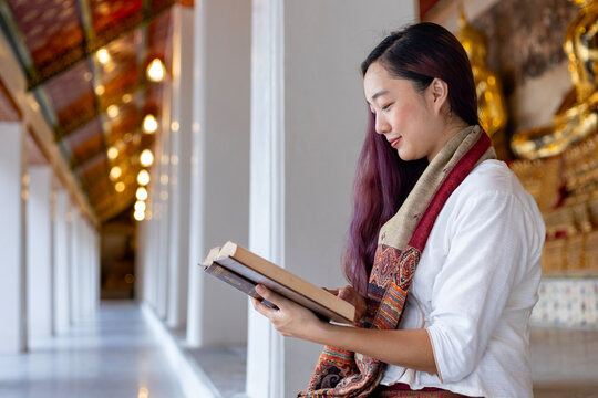 Asian buddhist woman is reading Sanskrit ancient Tripitaka book of Lord Buddha dhamma teaching while sitting in temple to chant and worship inside the monastery