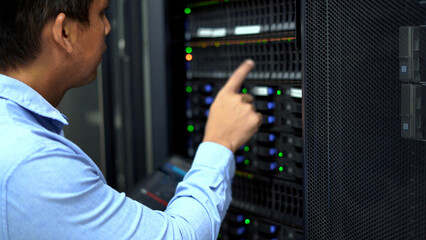 An IT professional in a blue shirt manages and monitors network servers in a data center, ensuring system stability and security.
