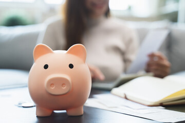 Young woman saving money monthly expenses putting coin in to piggy bank on the table.