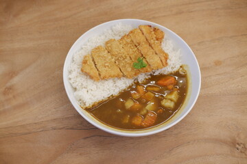 Rice with curry and chicken cutlet in white bowl on wooden table
